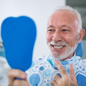 Older man in dental chair smiling at his reflection in handheld mirror