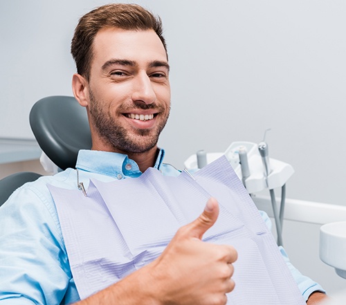 Male dental patient sitting in chair giving thumbs up