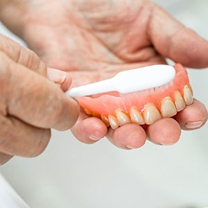 Person using a toothbrush to clean their dentures