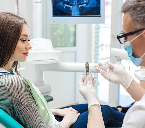 Dentist showing a model implant to a patient with long brown hair