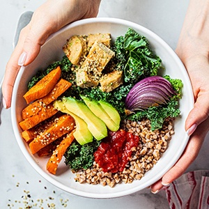 Bird’s eye view of two hands holding a large white bowl full of healthy salad ingredients over a marble counter with a fork