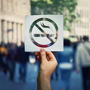 No smoking sign cutout held over a crowd of people on a street outside