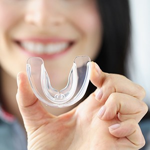 Clear mouthguard being held up by a woman whose face is blurry in the background