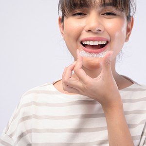 Smiling woman holding Invisalign aligner