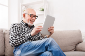 Older man smiling while reading untrue facts about dental implants on ipad